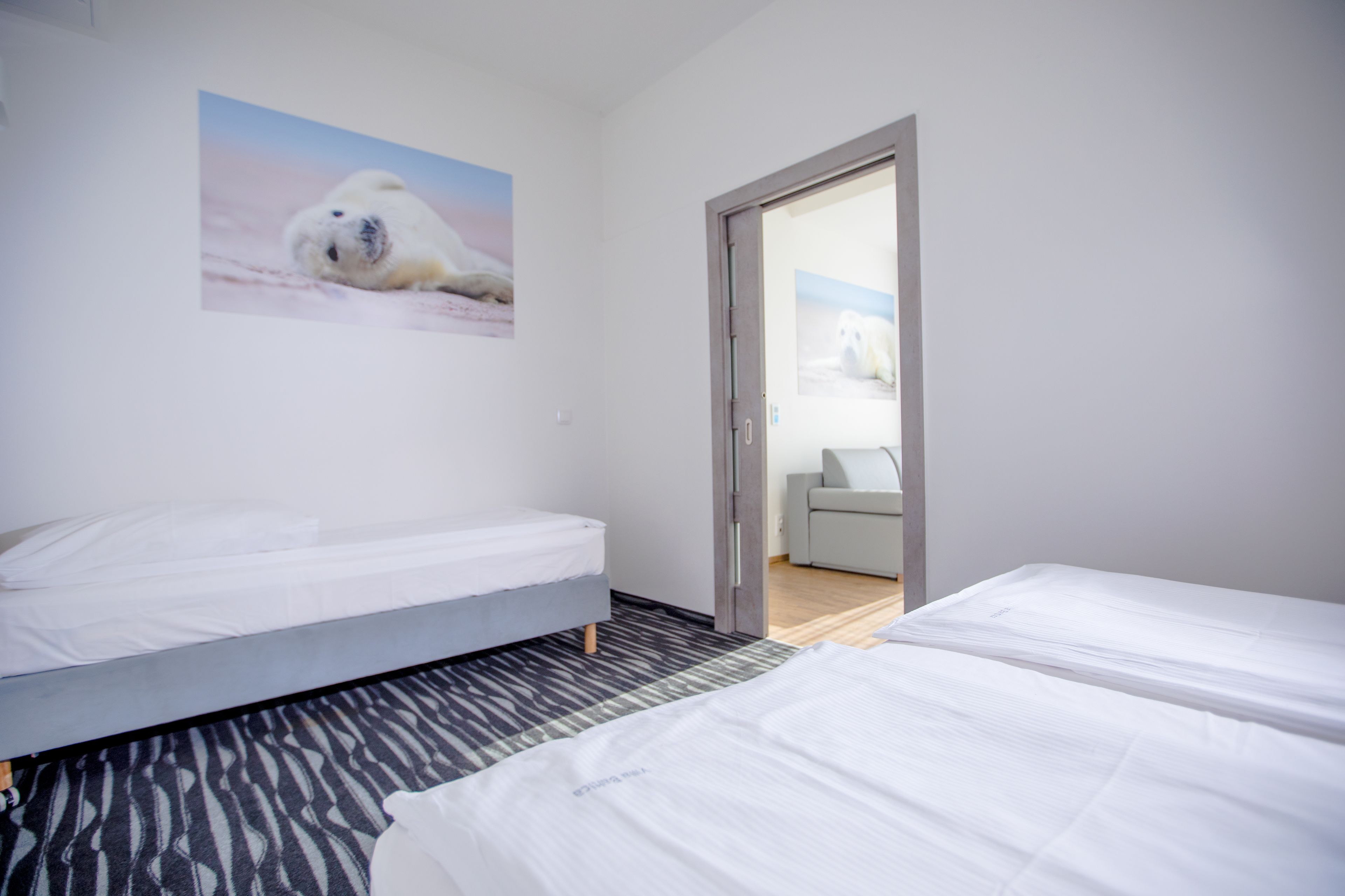 A hotel room with two beds, a polar bear picture on the wall, and a view of the room through an open door.