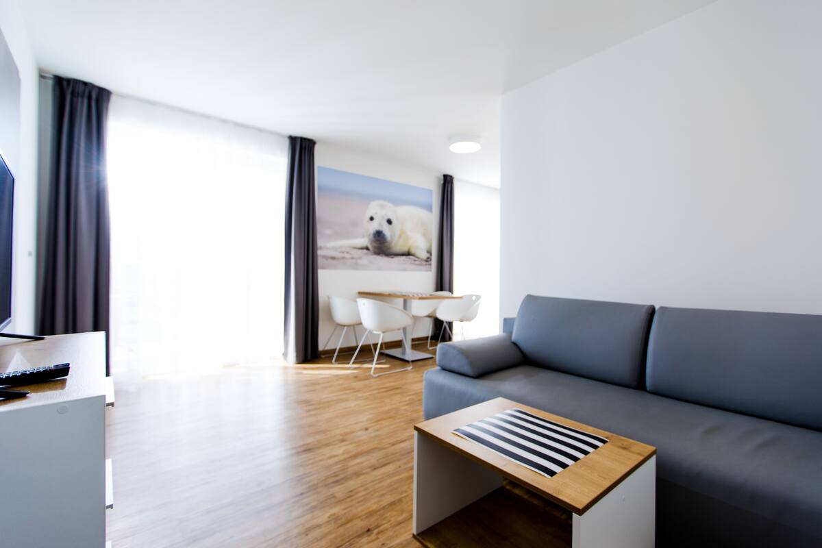 A modern living room with a grey sofa, a wooden coffee table, a TV, and a painting of a polar bear on the wall.