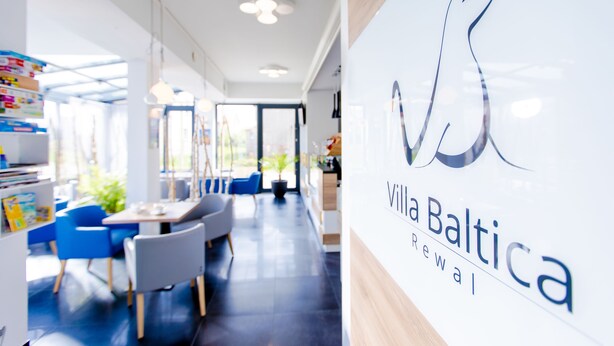 Un interior moderno con una zona de recepción, sillas azules y el logotipo de Villa Baltica Rewal.