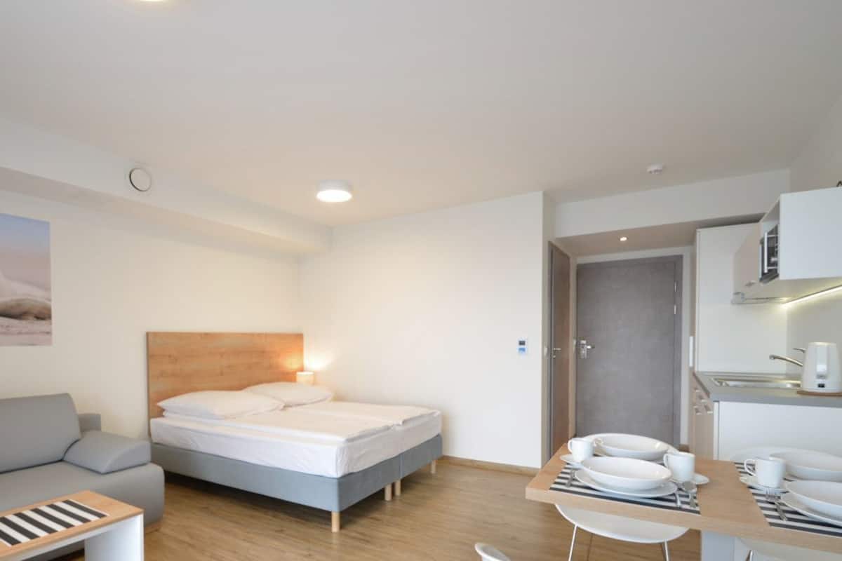 A modern hotel room with a bed, a sofa, a dining table with plates and cups, and a painting of a polar bear on the wall.