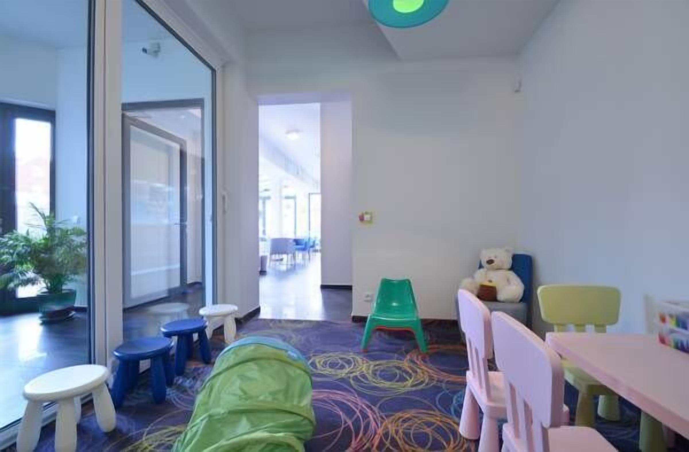 A children's playroom with colorful flooring, small stools, and a green chair.