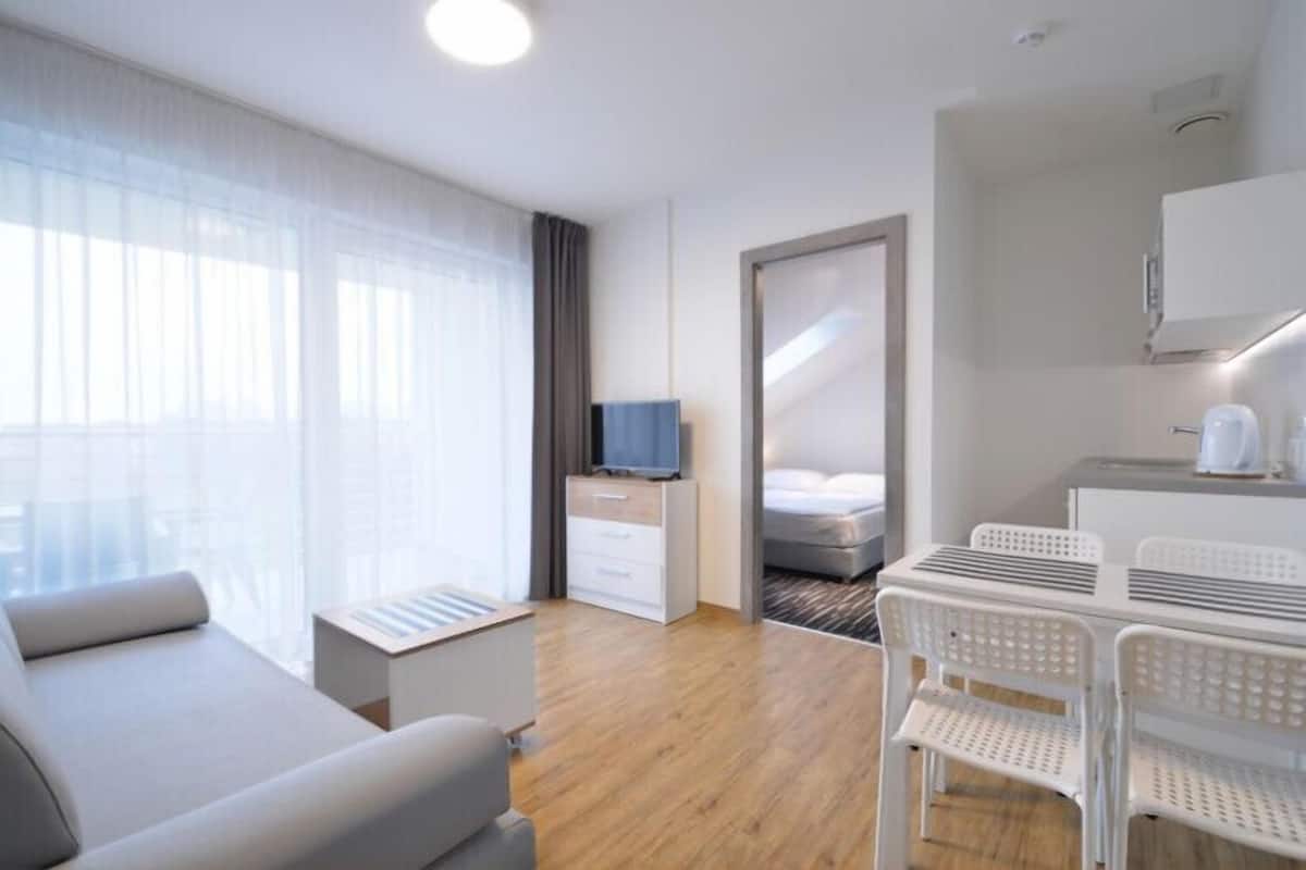 A modern hotel room with a sofa, a TV, a bed, a desk, and a chair.