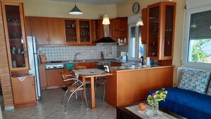 A compact kitchen with wooden cabinets, a dining area with chairs, a small island, and a sofa with a view.
