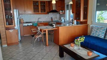 A compact kitchen with wooden cabinets, a dining area with chairs, a small island, and a sofa with a view.