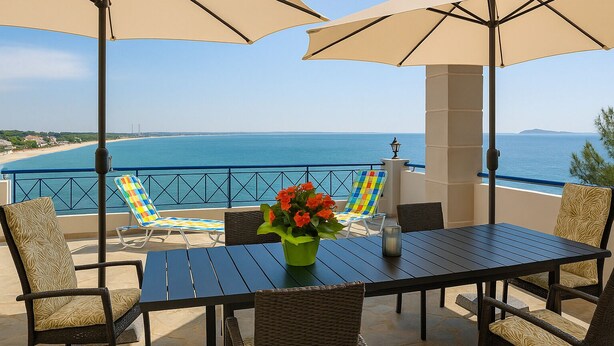 A terrace with a table, chairs, and umbrellas overlooking a beach and sea.