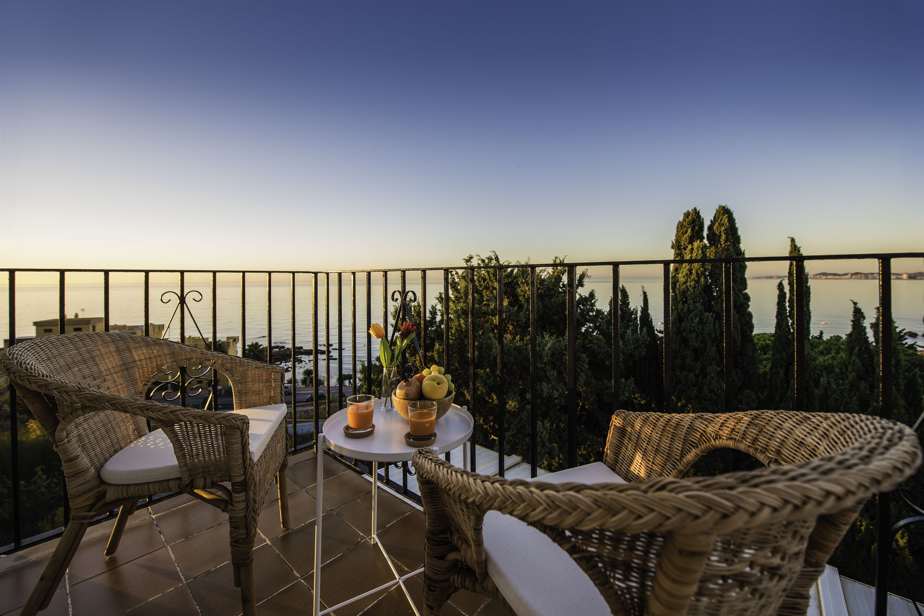Un balcon agrémenté de meubles en osier, une table avec des boissons et une vue sur les arbres et l’eau.