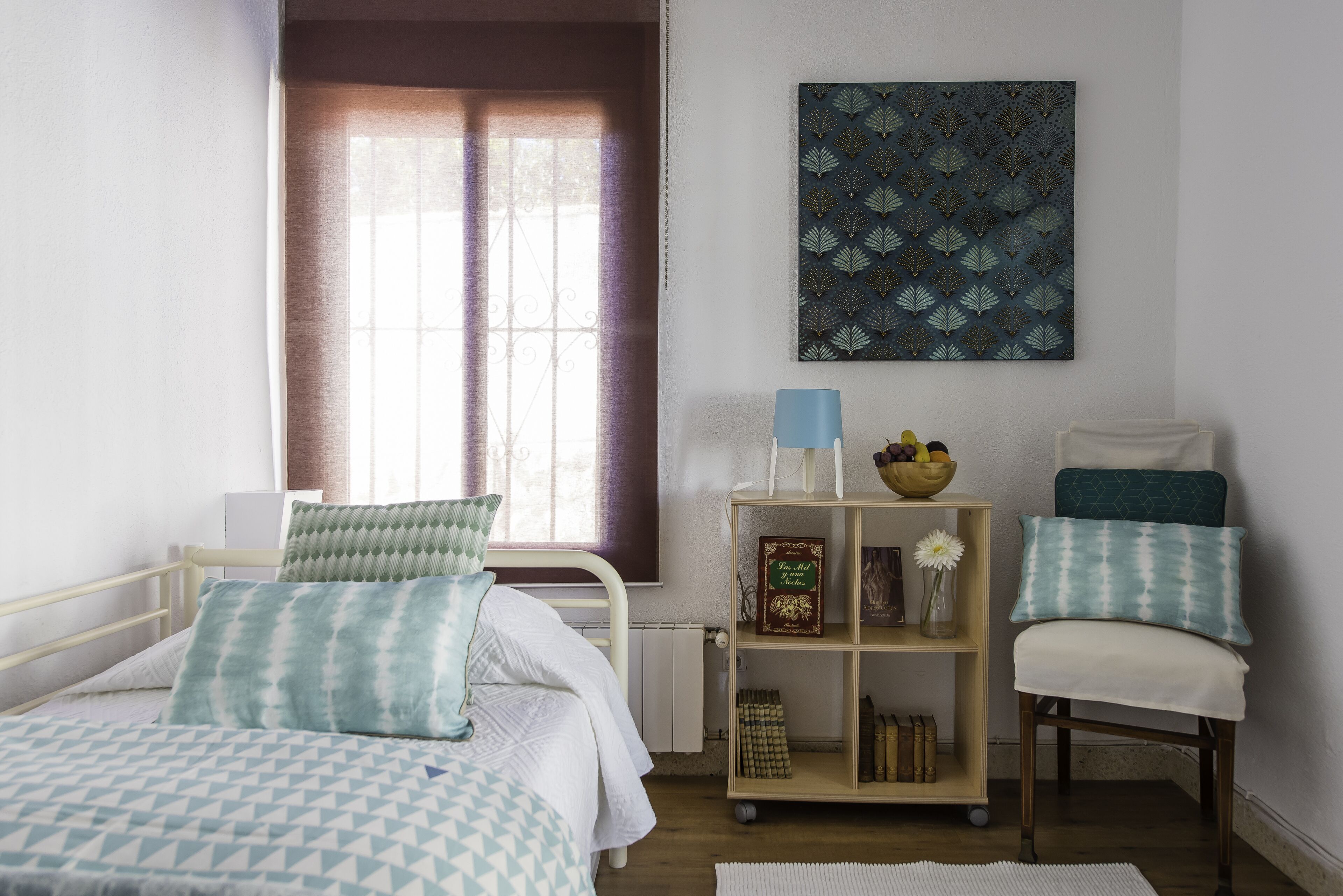 A bedroom with a bed, a chair, a bookshelf, and a window with curtains.