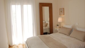 A hotel room with a large bed, a bedside table with a lamp, a mirror, and a window with sheer curtains. - Vilamoura dream vacation with fantastic beaches, golf courses and marina (Quarteira)