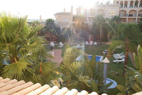 A resort courtyard with lounge chairs, palm trees, a pool, and a building with balconies.