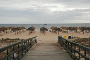 A wooden boardwalk leading to a beach with thatched umbrellas and beach chairs.