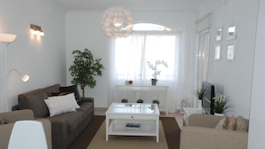 A modern living room with a glass coffee table, a sofa, a TV, and a large window with sheer curtains. - Vilamoura dream vacation with fantastic beaches, golf courses and marina (Quarteira)