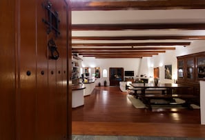 A spacious kitchen with wooden beams, a dining area with a large table, and a view of the living room. - Aquaria Villa (Santorini)