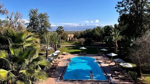 Une piscine entourée d’arbres, avec des chaises longues et des parasols, et offrant une vue sur les montagnes.