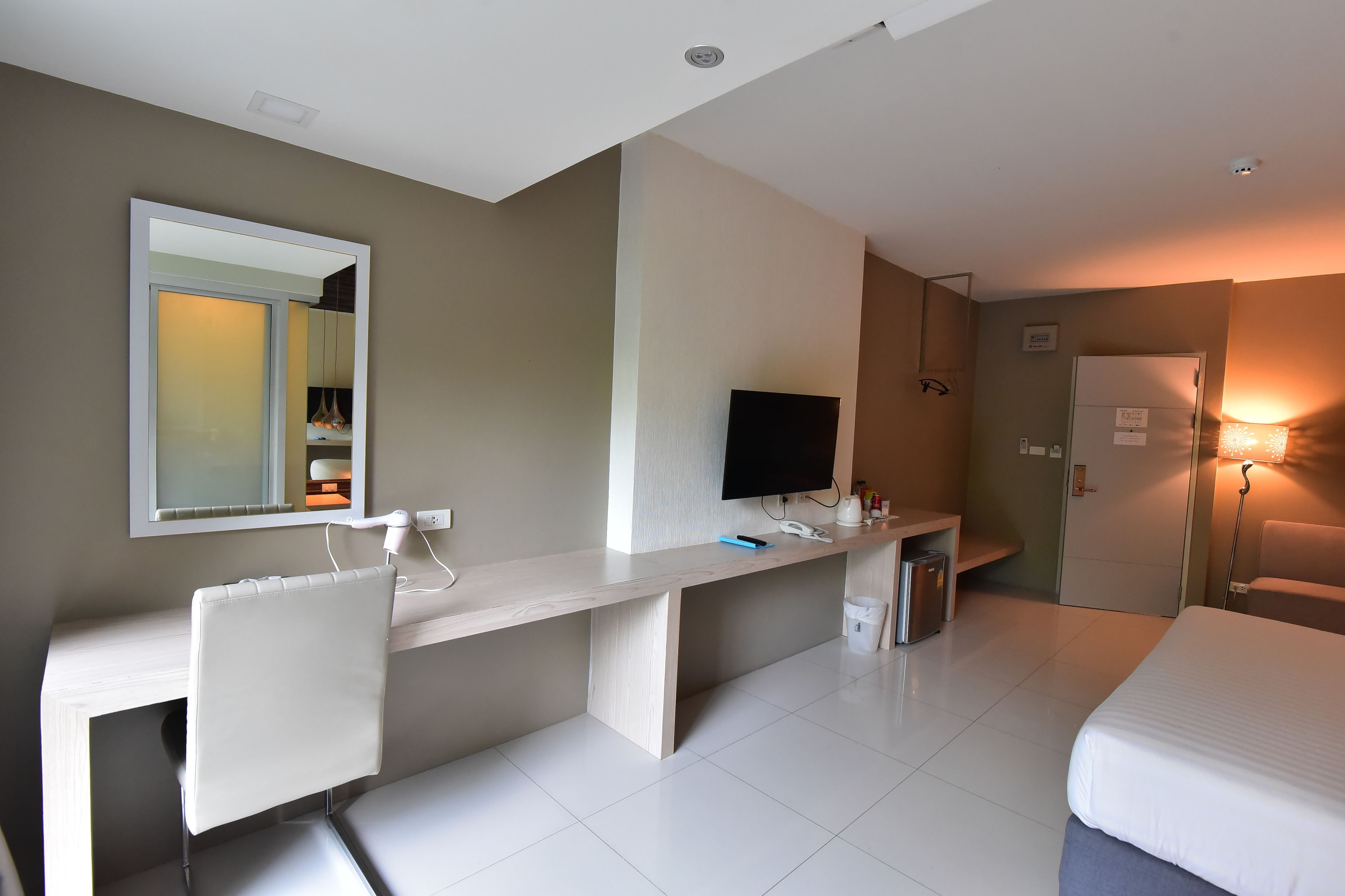 A modern hotel room with a bed, desk, chair, TV, and a mirror.