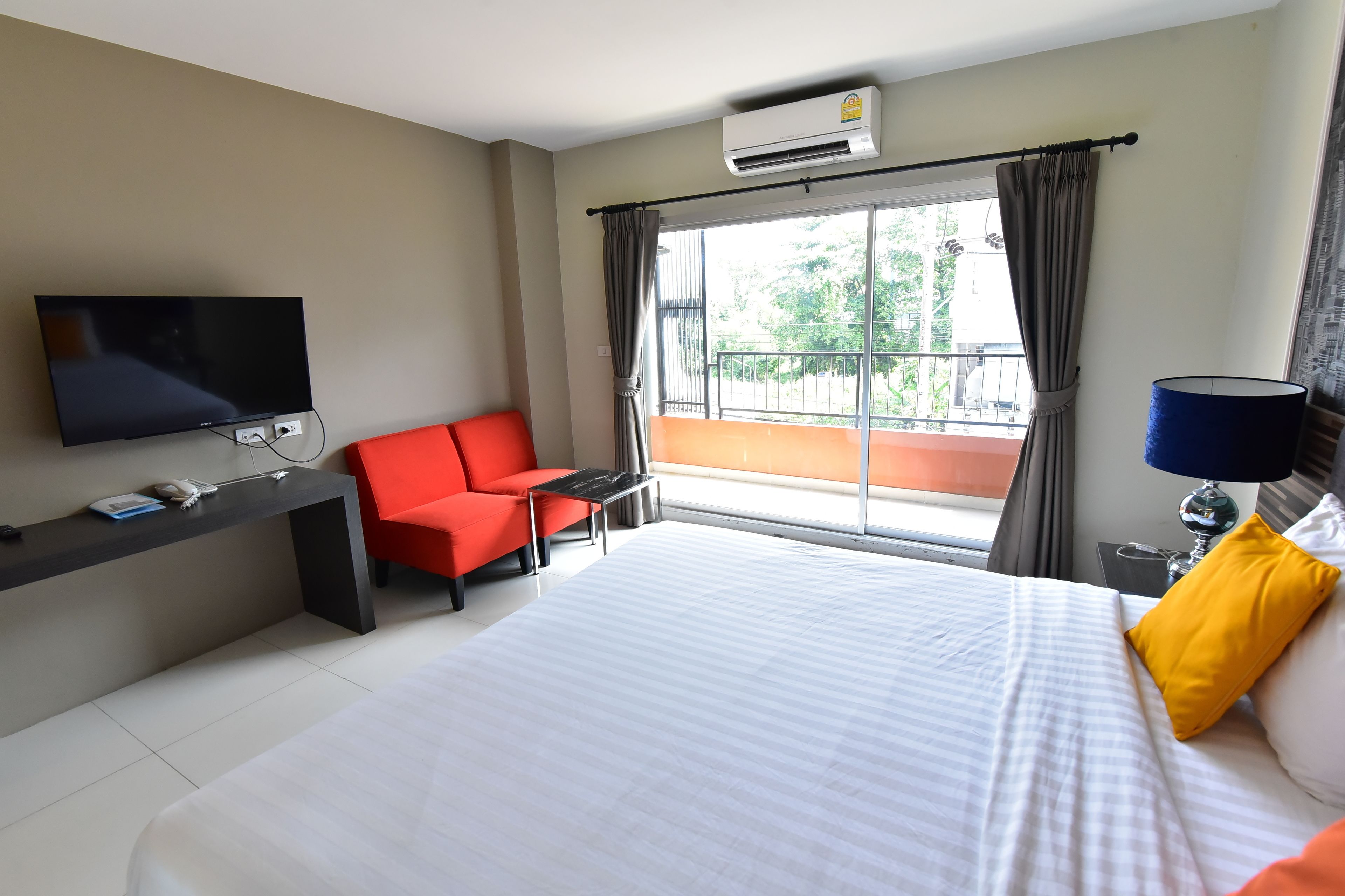 Una habitación de hotel con cama, televisión, escritorio, silla y balcón con cortinas.