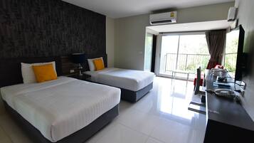 A hotel room with two beds, a desk, a chair, a TV, and an air conditioning unit.