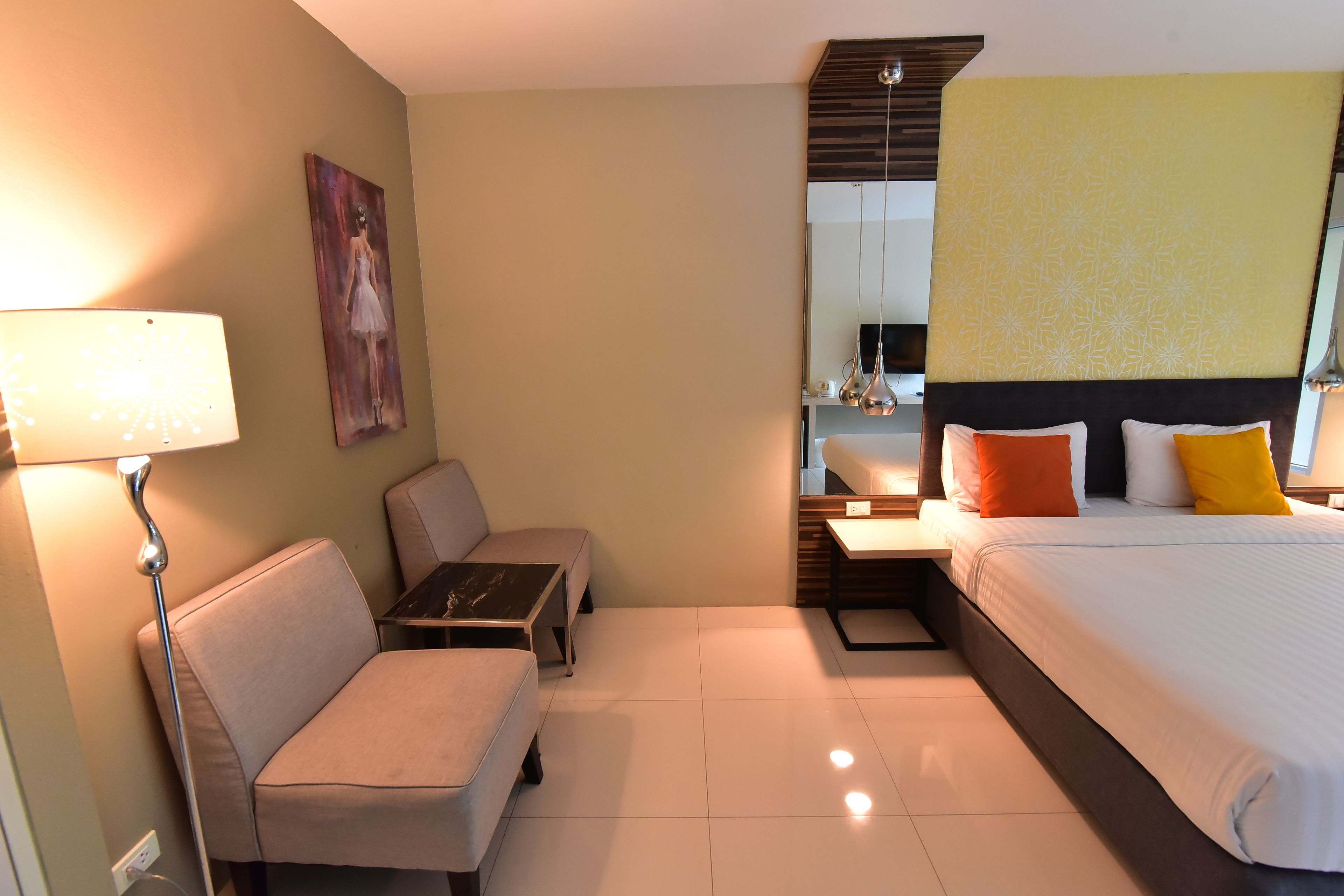 Una habitación de hotel con cama, sofá, una mesita, lámpara, un cuadro en la pared y un espejo sobre la cama.