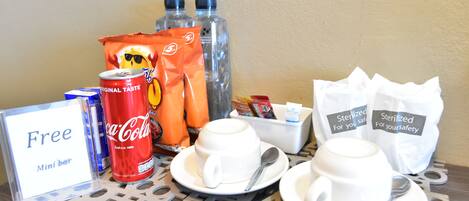 A mini bar setup with Coca-Cola, bottled water, snacks, and sterilized napkins.
