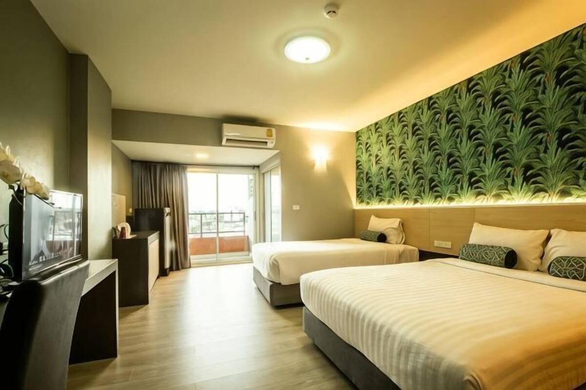 A hotel room with two beds, a desk, a TV, and a balcony with curtains.