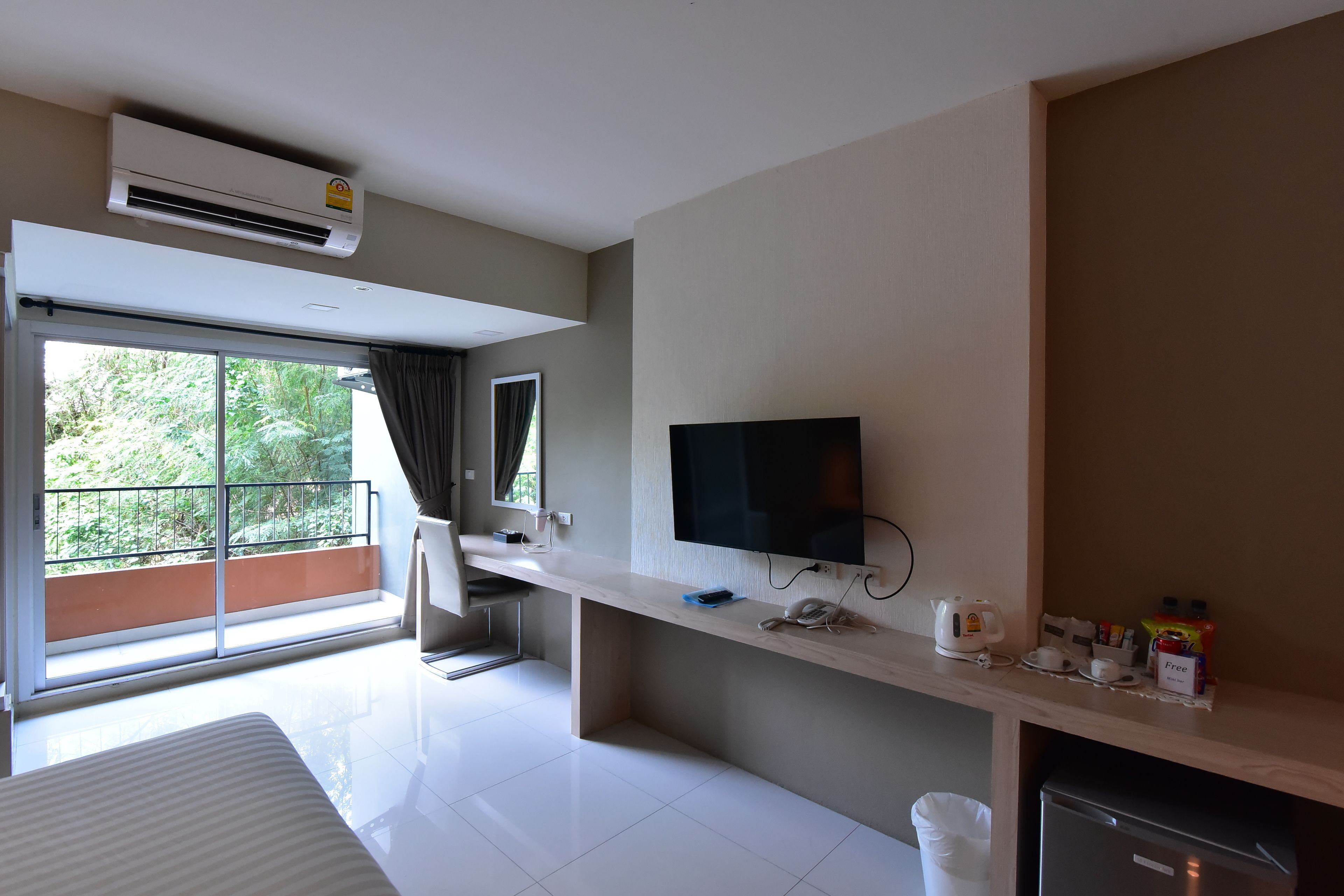 A modern hotel room with a large window, a flat-screen TV, a minibar, and a refrigerator.