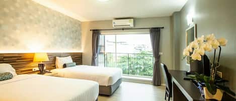A hotel room with two beds, a desk, a chair, a lamp, and a large window with a view of the outside.