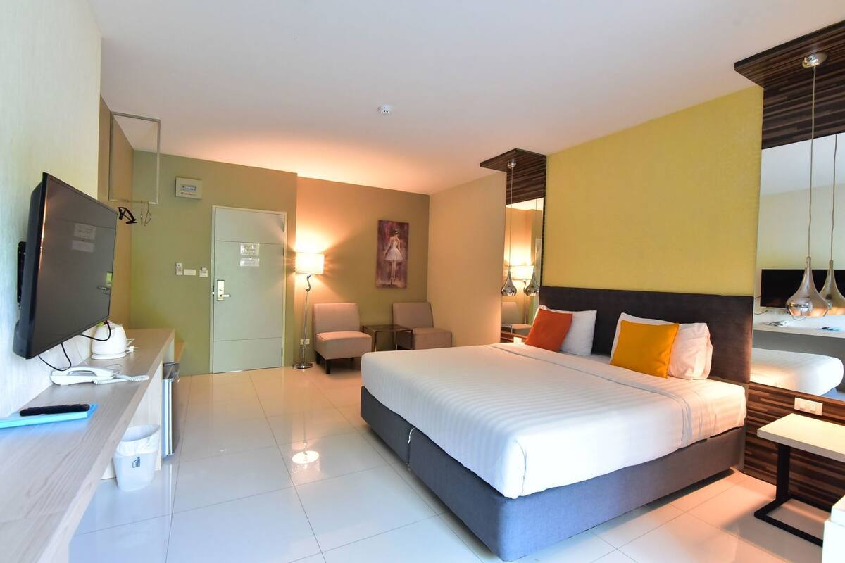 A hotel room with a bed, bedside table, lamp, TV, and a desk with a telephone.