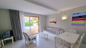 Una habitación con sofá, una mesa de comedor, sillas, televisión y un ventanal corredero que da a un área exterior.