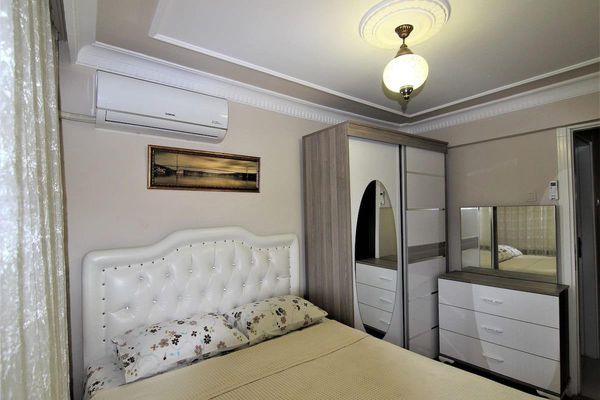 A bedroom with a bed, a wardrobe, a mirror, and an air conditioning unit.