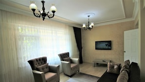 A living room with two armchairs, a sofa, a television mounted on the wall, and a chandelier. - Yılmaz Apart (Istanbul)