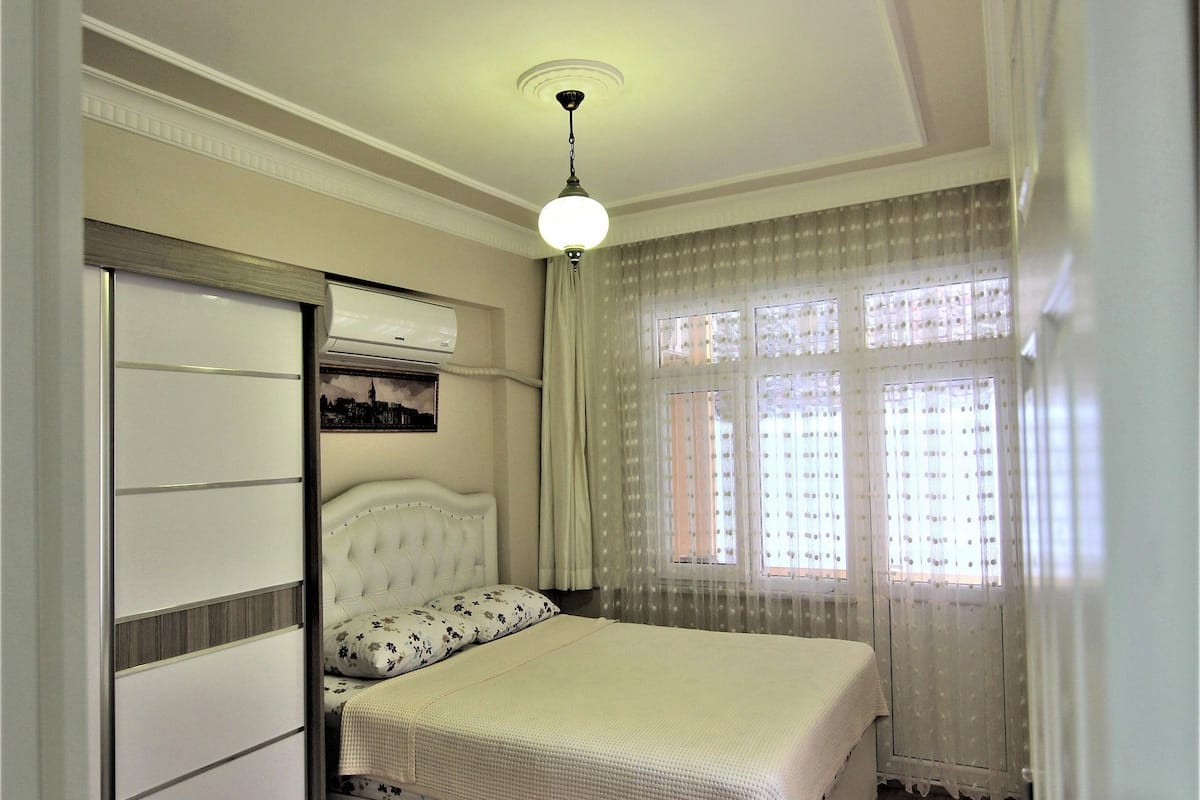 A bedroom with a bed, a wardrobe, a ceiling fan, and a window with curtains.
