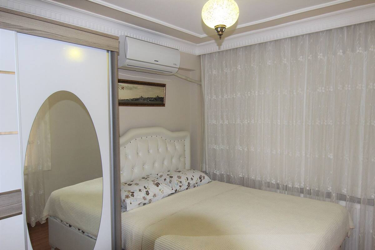A bedroom with a bed, a wardrobe, an air conditioning unit, and a ceiling light.