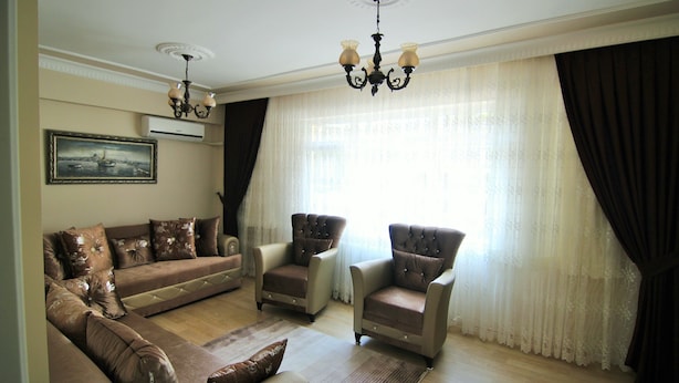 A living room with a brown sofa set, two armchairs, a chandelier, and a large window with curtains. - Yılmaz Apart (Istanbul)