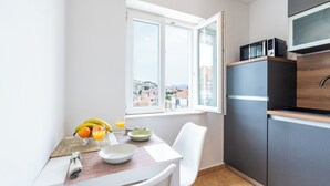 Eine kleine Küche mit Esstisch, einem Fenster mit Blick auf Gebäude und einer Mikrowelle über den Schränken.