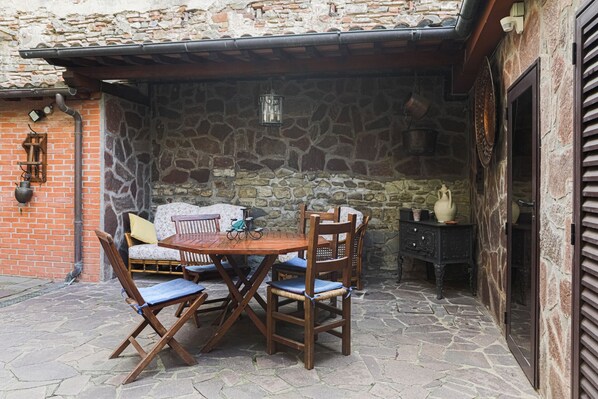 A stone-walled outdoor patio with a wooden table and chairs, a lantern, and a rustic wall-mounted cabinet.
