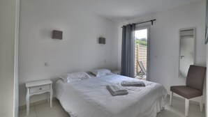 A bedroom with a bed, a chair, a nightstand, and a window with curtains. - Villa 4 by Avecoeur (Saint-Augustin)