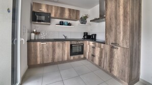 A modern kitchen with wooden cabinets, a built-in oven, a microwave, and a coffee maker. - Villa 4 by Avecoeur (Saint-Augustin)