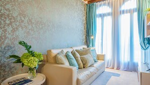 A living room with a sofa, a side table with a book, a vase with flowers, and a window with curtains. - Ca' Del Monastero 5 Collection (Venice)