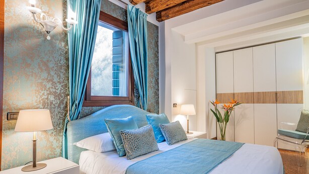 A bedroom with a bed, nightstands, a lamp, a window with curtains, and a mirror. - Ca' Del Monastero 5 Collection (Venice)