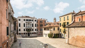 A courtyard with buildings on either side, a person walking, and a fountain in the center. - Ca' Del Monastero 5 Collection (Venice)