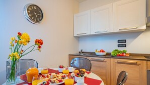 A modern kitchen with white cabinets, a clock, and a dining area with a red table set for breakfast. - Ca' Del Monastero 5 Collection (Venice)
