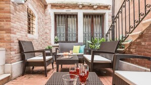 An outdoor seating area with wicker furniture, a table with drinks, and a brick wall. - Ca' Del Monastero 5 Collection (Venice)