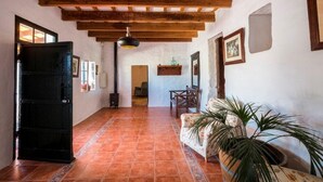 A hallway with a tiled floor, wooden ceiling beams, a black door, a sofa, and a potted plant. - Nice typical Menorcan house, with good location (es mercadal)