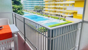 A balcony with a pool, white chairs, and a table with a fruit bowl. - Charming studio with shared pools (Bibione)