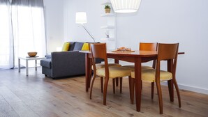 Un comedor con mesa y sillas de madera, un sofá con cojines, una mesita auxiliar y una lámpara de pie.