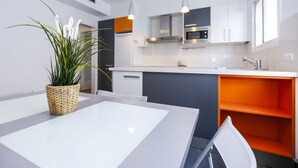 Una cocina moderna con armarios blancos, una pared de acento naranja y una zona de comedor con una mesa y una silla blancos.