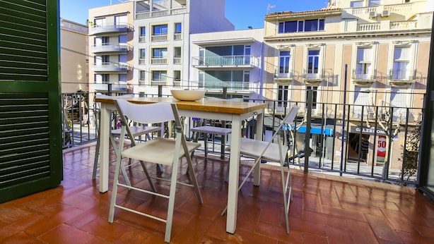 Un balcón con una mesa y sillas, con vista a un paisaje urbano con edificios de varios pisos.