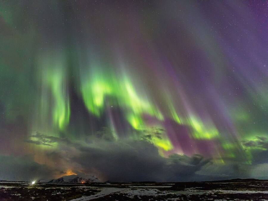Paesaggio innevato con una montagna sullo sfondo e l'aurora boreale nel cielo.