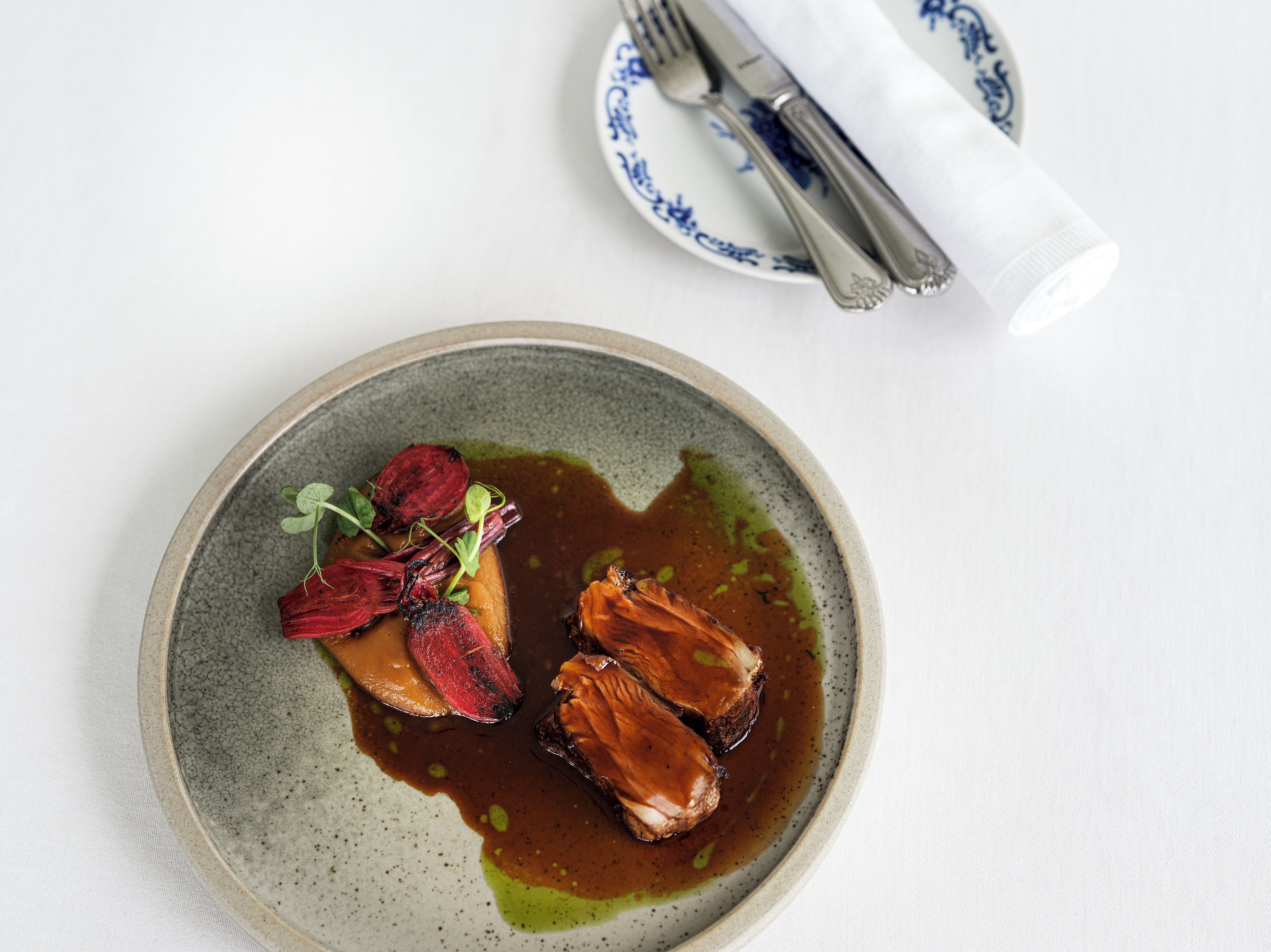 A plate with food and a napkin with cutlery on a table.