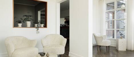 A spacious living room with two plush armchairs, a small wooden coffee table, and a large mirror on the wall.