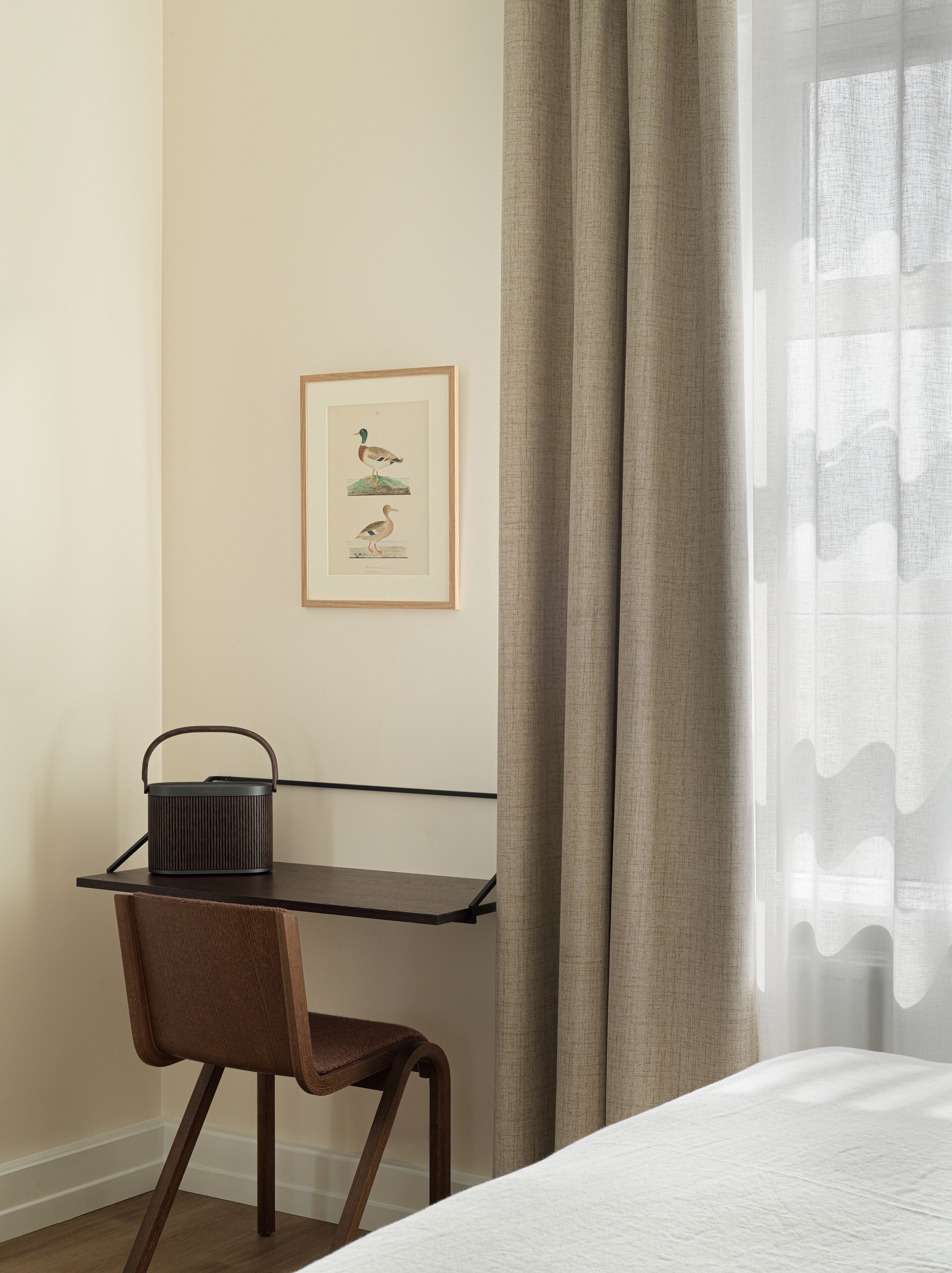 Una habitación de hotel ordenada con un escritorio de madera, una silla, una cama y una ilustración enmarcada en la pared.